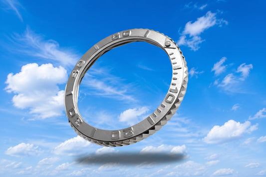 Edelstahllünette mit Relief-Alu-Insert in Silver – Schrägansicht mit diagonaler Rifflung vor blauem Himmel mit Wolken